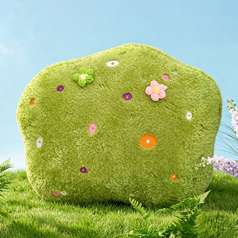 An aesthetic irregular-shaped green plush cushion resembling a soft patch of grass or moss, decorated with tiny colorful flowers, ideal as a cozy floor pillow or aesthetic room accent.