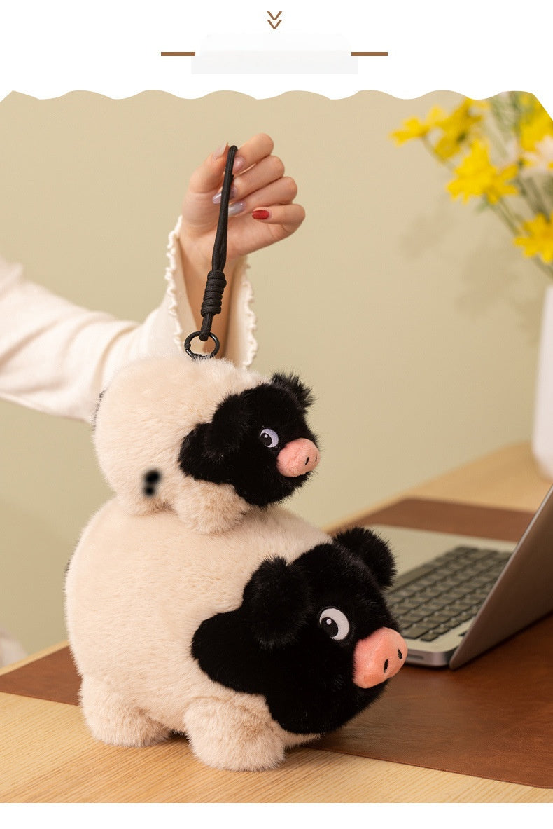 Pig Plush  keychain held by a hand on a desk with a laptop and flowers in the background.