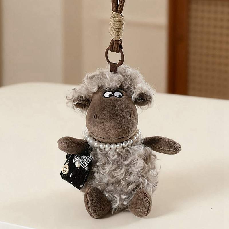 Kawaii mini sheep plush keychain with pearl necklace resting on a table for boutique B2B supply.