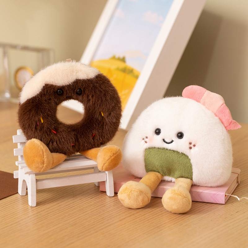 Bulk custom chocolate donut and onigiri rice ball plushies with dangling legs sitting on a white chair for retail vendors.