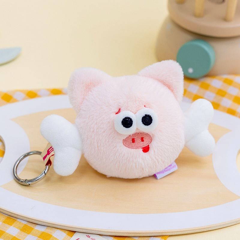 Factory-direct funny flying pig plush keychain on a wooden tray for B2B toy sourcing.