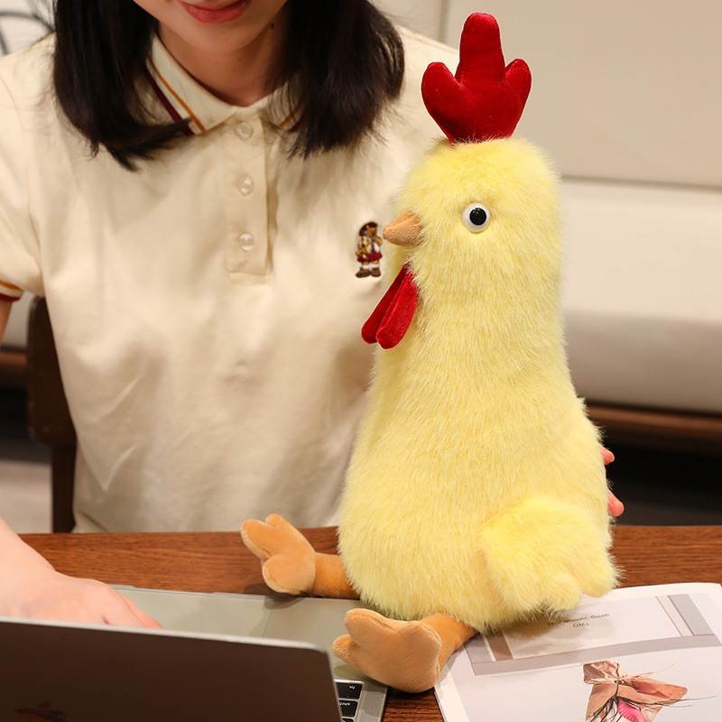 Yellow kawaii rooster plush toy sitting on a desk next to a laptop for retail distributors.