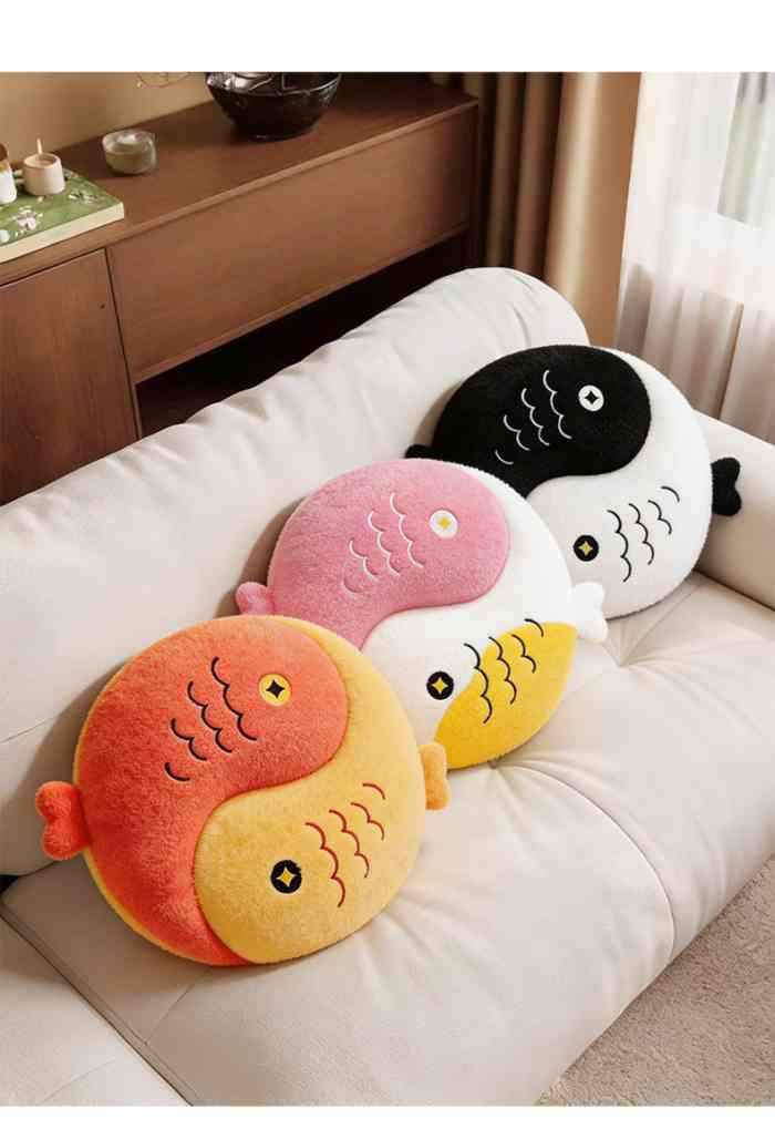 Orange, pink, and black Yin Yang lucky fish plush pillows neatly arranged on a modern white sofa.