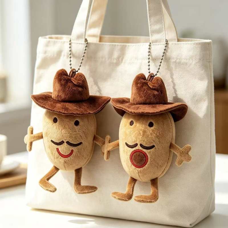 Pair of funny cowboy potato stuffed toy keyrings hanging on a beige canvas tote bag.