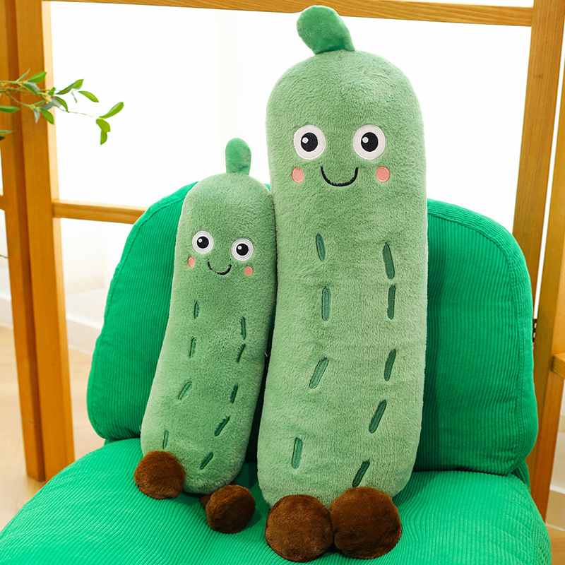 Two smiling cucumber stuffed animals sitting on a green chair, cute emotional support plushies for wholesale and home decor displays.