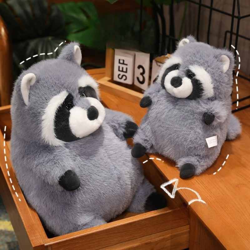 Two wholesale chubby raccoon plush toys sitting on a wooden desk, available for B2B sourcing.