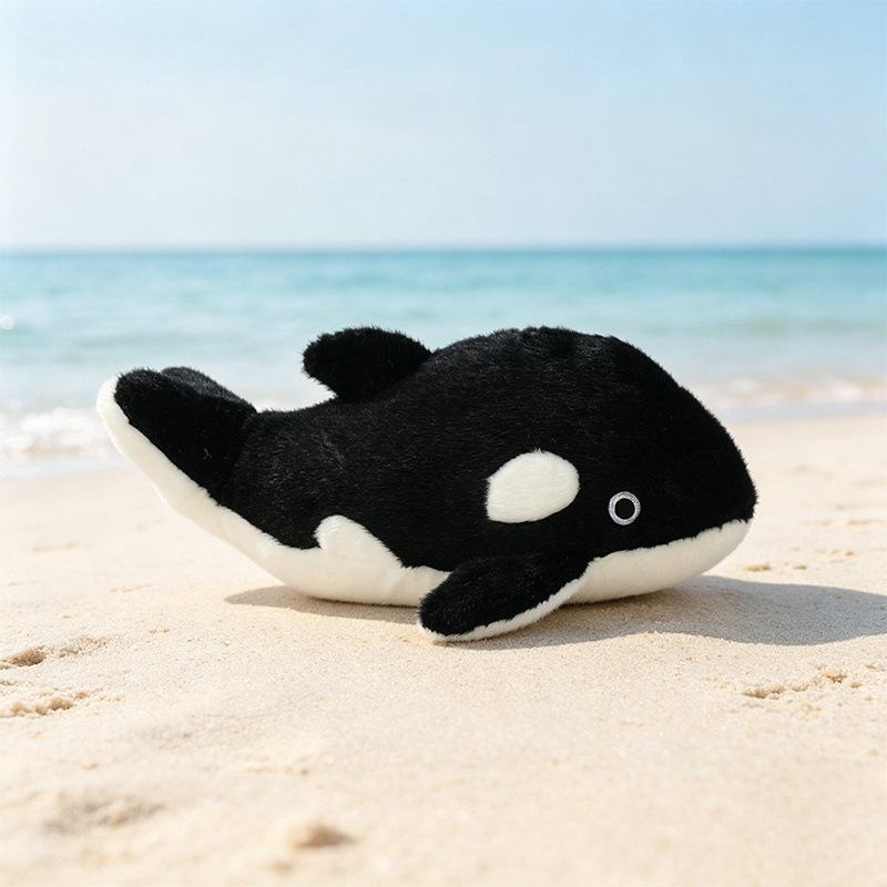 Wholesale killer whale orca plush toy resting on the beach sand for B2B procurement.