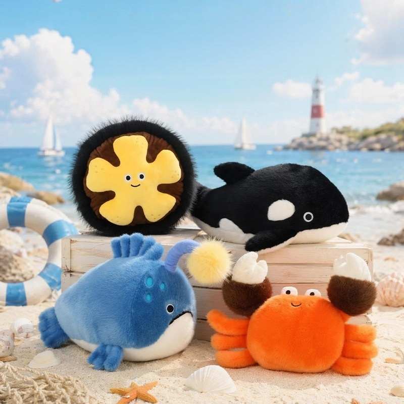 Wholesale ocean animal plush toy assortment including orca, crab, anglerfish, and starfish on a beach.